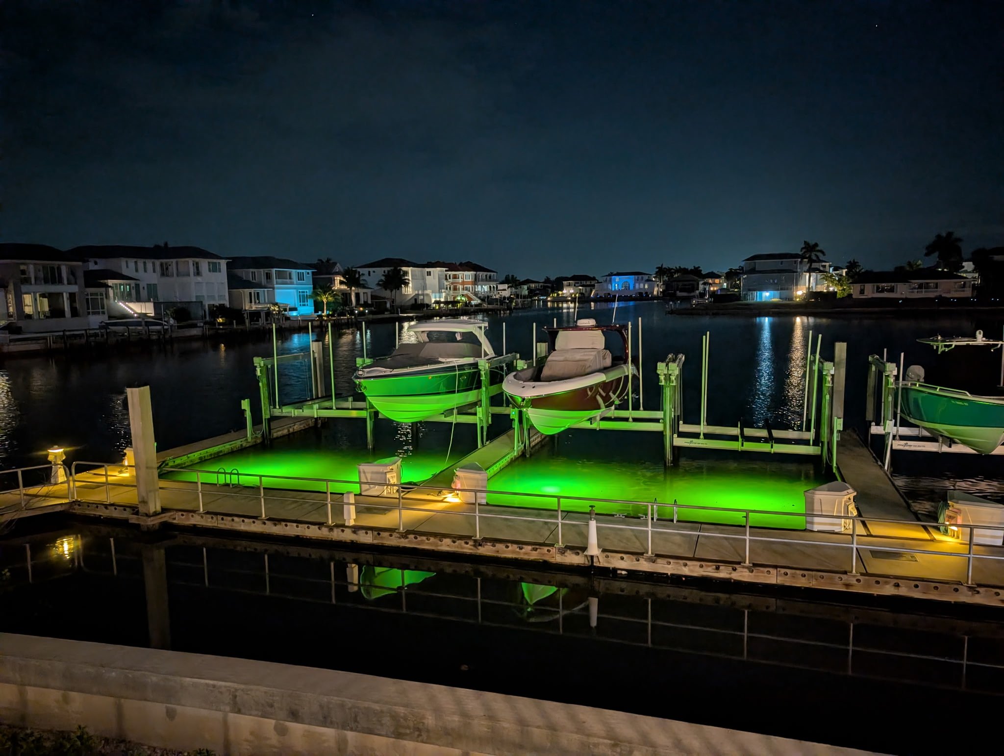 Boat slips at night lit bright green by underwater dock lights